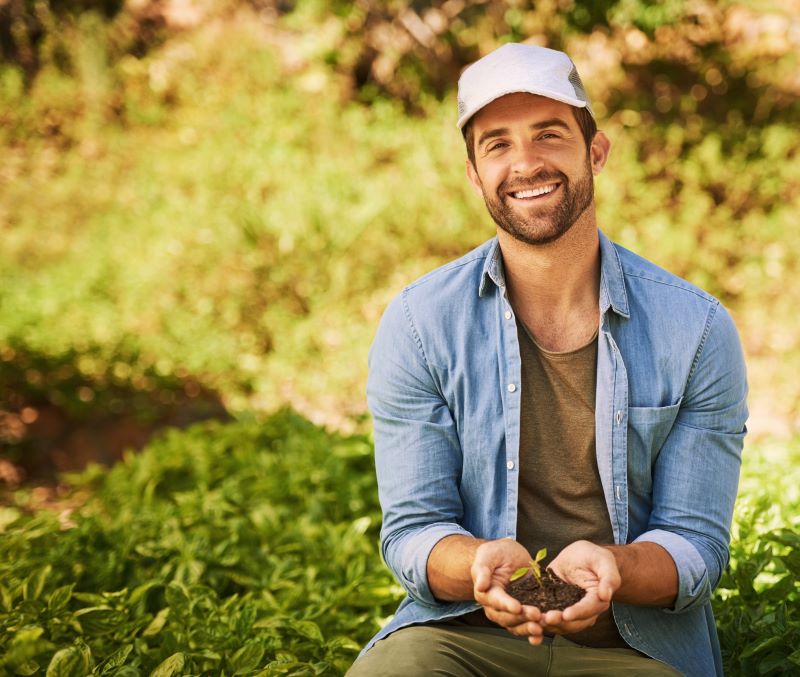 Homem produtor rural no campo segurando porção de terra nas mãos.